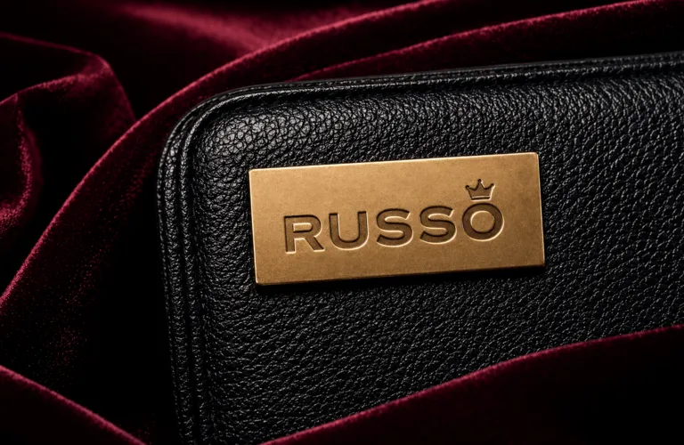 Placa metálica dorada grabada con logotipo Russo aplicada sobre cartera de piel negra